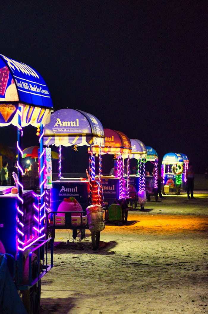Vibrant illuminated vending stalls on a sandy beach at night in Kolkata, India.